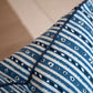 A close-up image of a 22" x 22" patterned blue and white custom Litani Blues Pillow by Associated Design with horizontal stripes and small geometric designs. The down-filled pillow features dark piping along the edges.