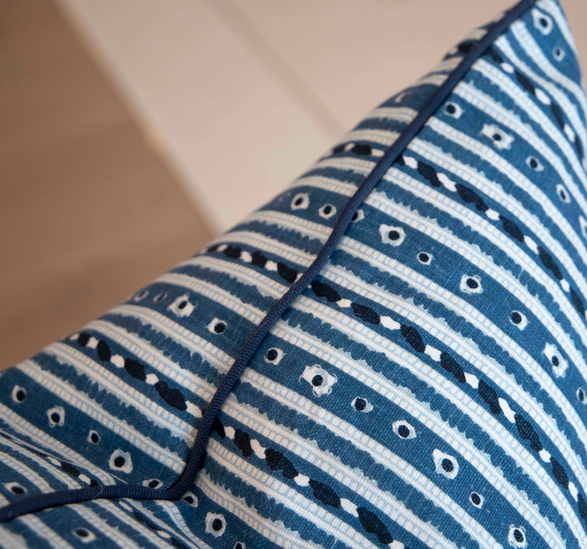A close-up image of a 22" x 22" patterned blue and white custom Litani Blues Pillow by Associated Design with horizontal stripes and small geometric designs. The down-filled pillow features dark piping along the edges.