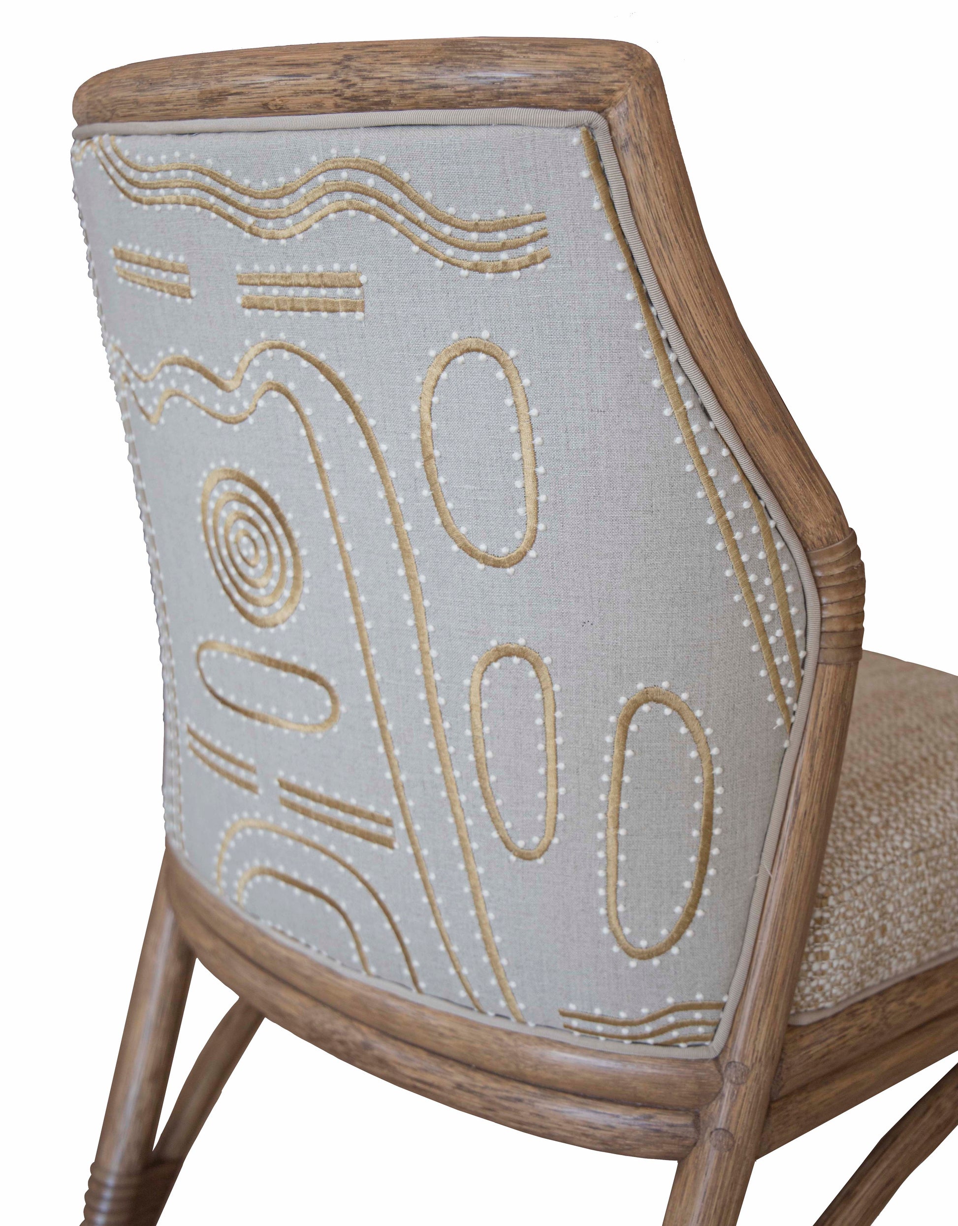 Close-up view of a McGuire Lantana Side Chair, Mushroom with intricate embroidery on the backrest, featuring abstract patterns in cream and beige tones, set within a light wooden frame. The furniture dimensions are 21.25"W and 23"D.