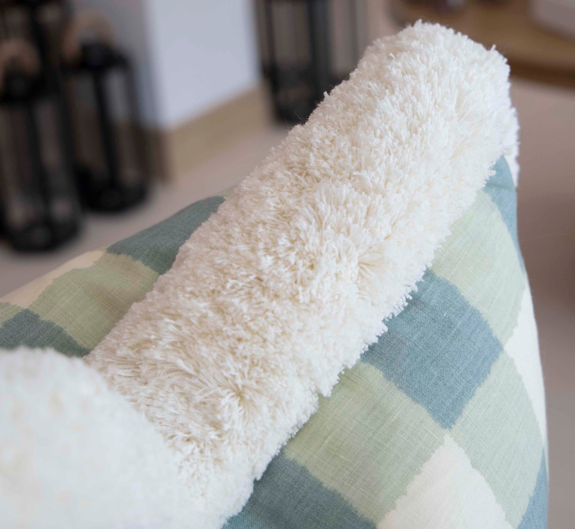 A close-up of a fluffy white blanket draped over the Hive Custom Pillows Small Check Blue Pillow.