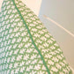 Close-up of the 22" x 22" Burma Meadow Outdoor Pillow by Hive Custom Pillows, featuring green fabric with a white leaf pattern and green piping along the edge.