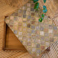 A decorative wooden box, the Bojay Diamond Box in Medium, featuring a diamond pattern and mother of pearl inlay is partially open on a bamboo mat, with a green plant extending into the frame.