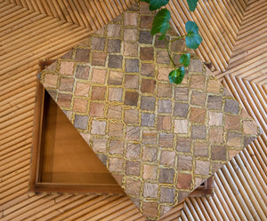 A decorative wooden box, the Bojay Diamond Box in Medium, featuring a diamond pattern and mother of pearl inlay is partially open on a bamboo mat, with a green plant extending into the frame.