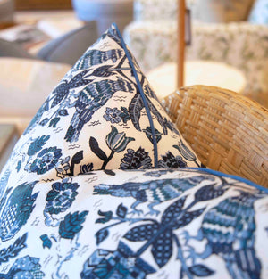 Close-up of the Damour Blues Pillow by Hive Custom Pillows, a handmade, down-filled cushion featuring a blue and white floral pattern, displayed on a woven chair. Crafted in the USA.