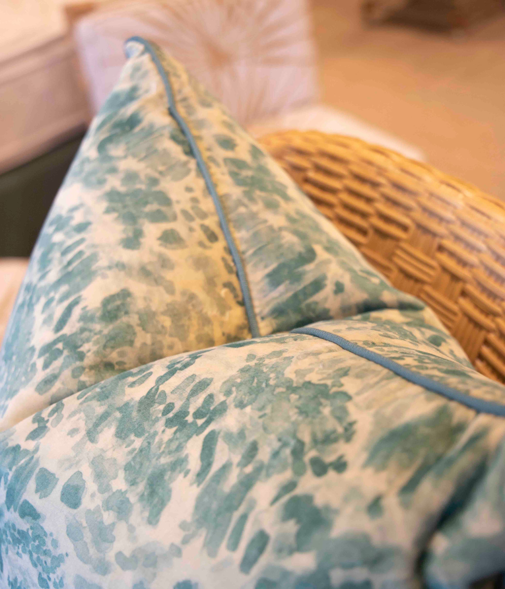 A close-up of a handmade wicker chair features the Heather Moss Pillow from Beleo Interiors LLC, with a decorative down-filled cushion showcasing a textured blue and white pattern, adding an artisanal touch to the scene.