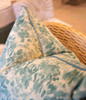 A close-up of a handmade wicker chair features the Heather Moss Pillow from Beleo Interiors LLC, with a decorative down-filled cushion showcasing a textured blue and white pattern, adding an artisanal touch to the scene.