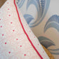 Close-up of the Pasha Ballet Pillow by Associated Design, featuring a custom-made patterned cover with red piping. Positioned against blue and white wave-patterned wallpaper, it is crafted from the finest materials.