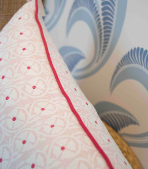Close-up of the Pasha Ballet Pillow by Associated Design, featuring a custom-made patterned cover with red piping. Positioned against blue and white wave-patterned wallpaper, it is crafted from the finest materials.