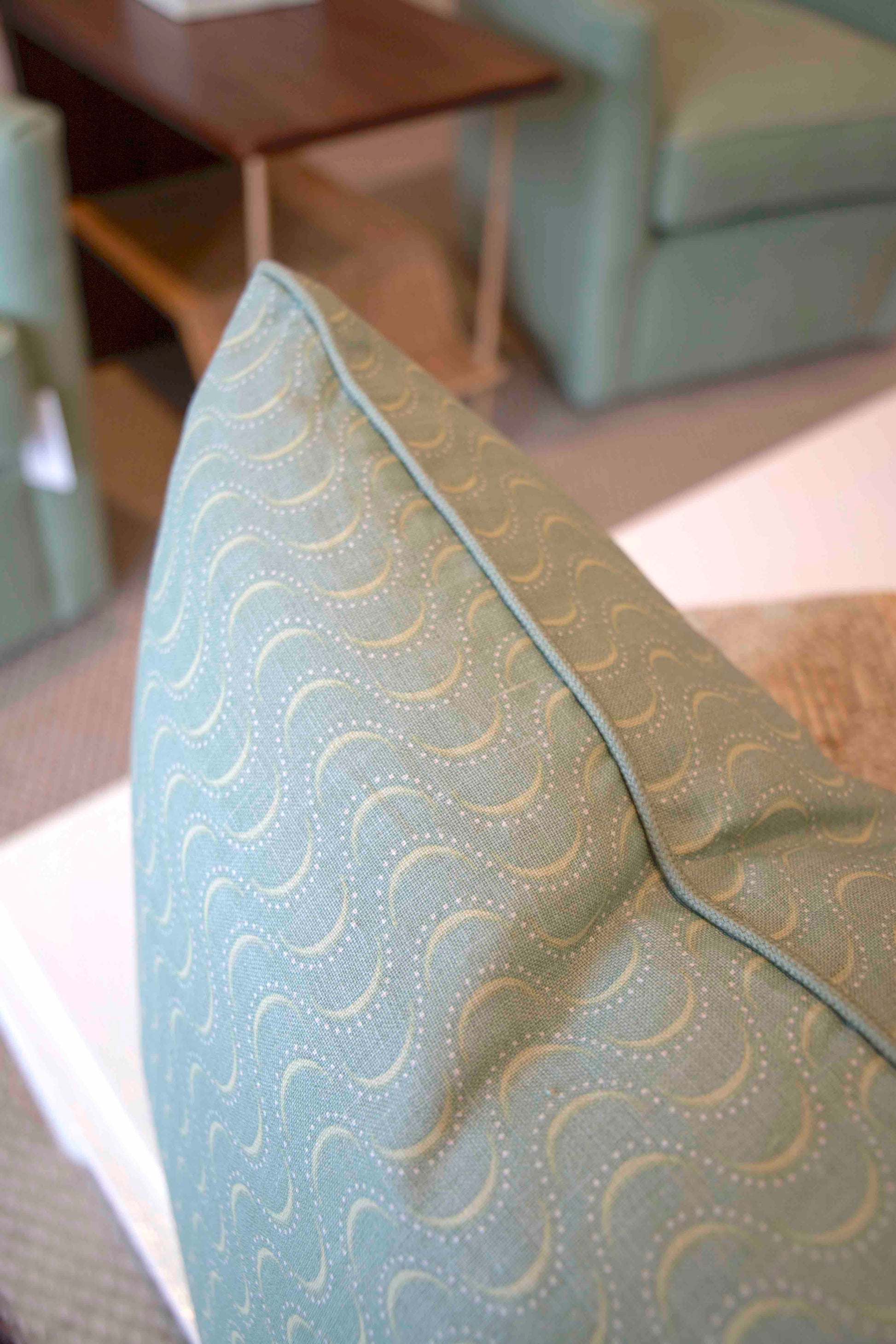 Close-up of the Ondine Soft Green Pillow by Hive Custom Pillows, featuring a wavy stitched pattern and displayed on a white surface in a living room.