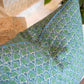 The Scopello Emerald Linen Pillow by Hive Custom Pillows, handmade in the USA with down filling and a blue-green leaf pattern, rests on a light surface beside a plant and woven decor.