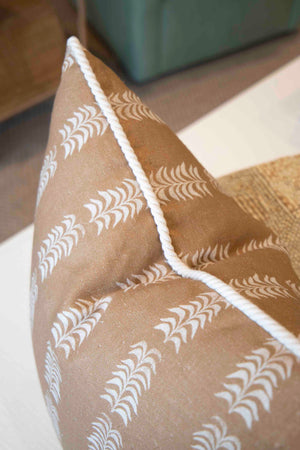 The Petite Frond Camel Pillow by Hive Custom Pillows is handmade in the USA with white leaf patterns and white piping on brown fabric, shown here on a light-colored surface.