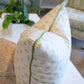 A close-up of the Dolly Flower Lettuce Green Pillow by Associated Design, featuring a light pattern and green piping, rests on a white table in a furnished living room. Handmade in the USA for an elegant touch.