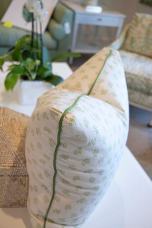 The Dolly Flower Lettuce Green Pillow by Hive Custom Pillows features a handmade, light-hued design with a green floral pattern and green piping, down-filled for comfort, displayed on a white table near a plant and furniture.