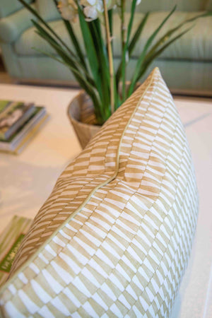Close-up of the Tane Golden Pillow by Hive Custom Pillows, a beige and white checkered, down-filled pillow handmade in the USA, shown on a white surface with a potted plant and magazines blurred in the background.