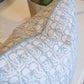 A close-up of the Ashok Duck Egg Pillow by Hive Custom Pillows, featuring blue and beige designs, sits near a potted plant on a white surface. This down-filled pillow adds cozy charm to any USA-inspired space.