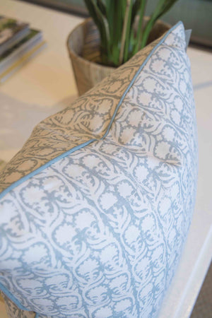 A close-up of the Ashok Duck Egg Pillow by Hive Custom Pillows, featuring blue and beige designs, sits near a potted plant on a white surface. This down-filled pillow adds cozy charm to any USA-inspired space.