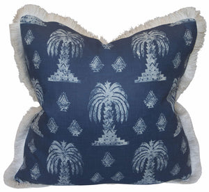 The Mandalay Indigo Pillow by Hive Custom Pillows is a square down-filled pillow with a navy cover featuring white palm tree and geometric patterns, light fringe trim, and is handmade in the USA for a stylish, cozy accent.