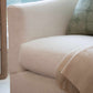 Close-up of Lee Industries Barrel Swivel Chair in beige, featuring a rounded back, a green patterned cushion, and a light fringed throw draped over the seat.