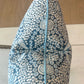 A close-up of the Shell Grotto Seaside Outdoor Pillow by Associated Design, showing its blue and white geometric pattern, central seam, light blue piping, and detailed craftsmanship.