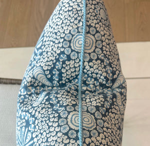 A close-up of the Shell Grotto Seaside Outdoor Pillow by Associated Design, showing its blue and white geometric pattern, central seam, light blue piping, and detailed craftsmanship.