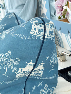 The Fall Pagoda Blue Pillow by Hive Custom Pillows features fine blue fabric with white Asian-inspired scenic prints and piping, perfectly complementing a partial vanity mirror and a pink orchid in the background.