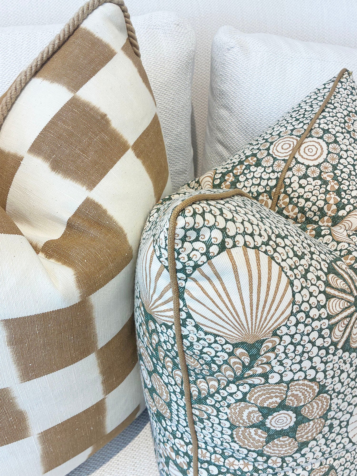 Two Associated Design Shell Grotto Green/Tan Pillows add style to a light couch, featuring elegant green and tan patterns and crafted from the finest materials.