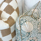 Two decorative throw pillows rest on a light couch: the Checkerboard Toffee Pillow from Hive Custom Pillows with a tan and white checkered pattern, and another pillow featuring a green and beige floral design.