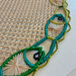 Close-up of the Mercedes Salazar Fish Dance Placemat featuring a beige lattice center and a vibrant stitched border in green, blue, and yellow.