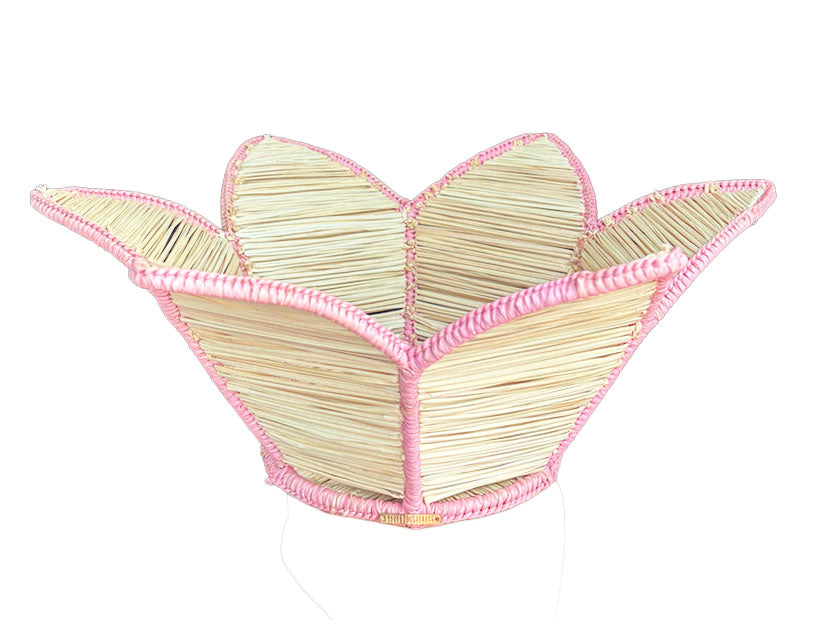 The Mercedes Salazar Pink Petals Basket is a woven raffia basket with five petal-shaped sections and pink trim, ideal for displaying tropical leaves.