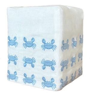 The Haute Home Mini Crab Bath Collection features a white fabric cube ottoman crafted from premium linen, adorned with a repeating pattern of blue crabs on its sides.