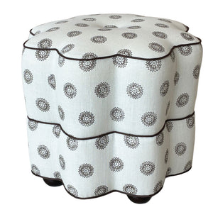 The Bunny Williams Stella Stool is a two-tiered, scalloped ottoman upholstered in white fabric with a black floral medallion print and dark edge piping.