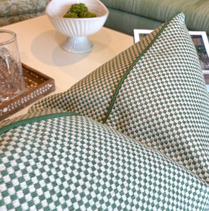 Two Associated Design Chequerboard Stitch Pillows in green and white are arranged on a sofa, accompanied by a bowl, tray, glass, and framed photo on a nearby table.