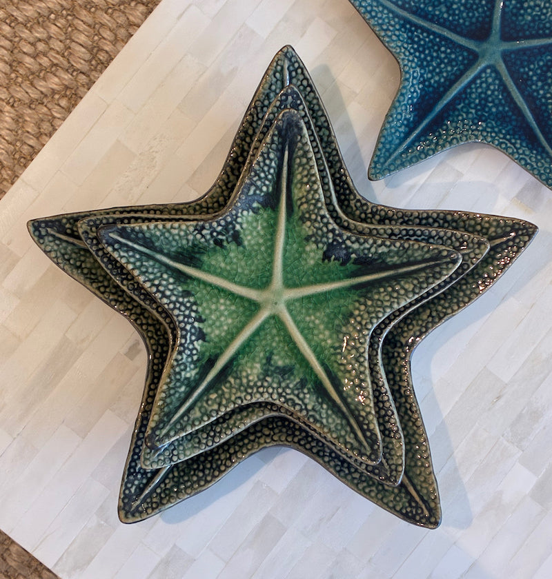 Three ceramic starfish-shaped plates from the Van Cleve Collection's Green Starfish Dish Collection feature a deep green glaze with blue tones, stacked on a white tiled surface.