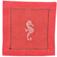 The Coastal Cocktail Napkin Set by Pink House Mustique features pink linen napkins with a central embroidered white seahorse and a decorative border.