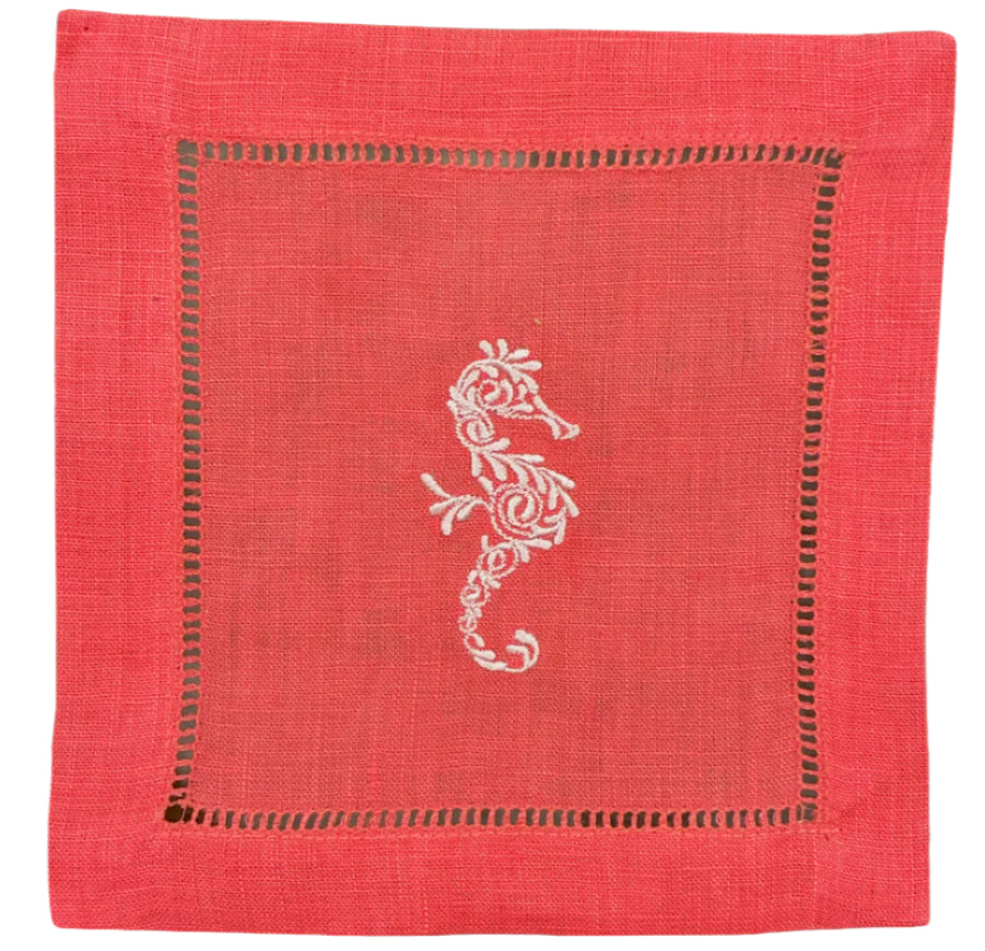 The Coastal Cocktail Napkin Set by Pink House Mustique features pink linen napkins with a central embroidered white seahorse and a decorative border.