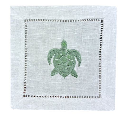 The Coastal Cocktail Napkin Set by Pink House Mustique features white linen napkins with a green embroidered turtle and cutwork hemstitch—ideal for adding seaside charm to your table.