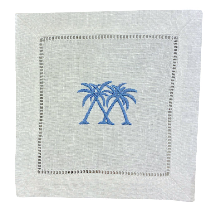 The Coastal Cocktail Napkin Set by Pink House Mustique features white linen napkins with two blue embroidered palm trees at the center and a decorative hemstitch border.