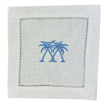 The Coastal Cocktail Napkin Set by Pink House Mustique features white linen napkins with two blue embroidered palm trees at the center and a decorative hemstitch border.