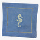 The Coastal Cocktail Napkin Set by Pink House Mustique features blue linen napkins with a decorative yellow embroidered seahorse at the center and elegant openwork stitching details.