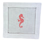 The Coastal Cocktail Napkin Set by Pink House Mustique features white linen napkins with a cutwork border and a red embroidered seahorse, bringing a coastal flair to your table.