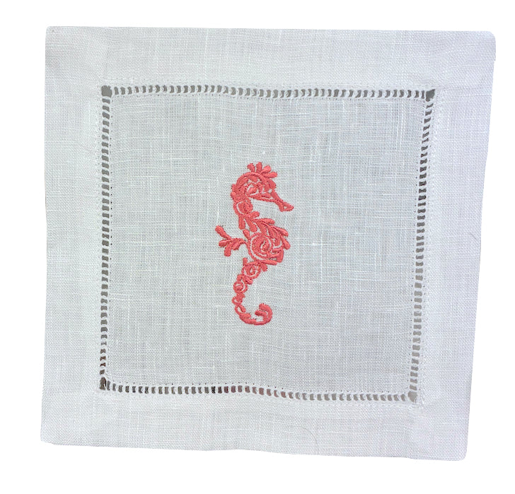 The Coastal Cocktail Napkin Set by Pink House Mustique features white linen napkins with a cutwork border and a red embroidered seahorse, bringing a coastal flair to your table.