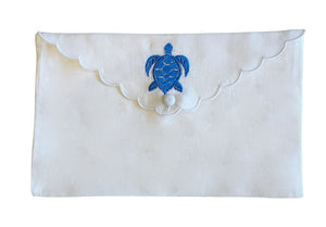 From the Pink House Mustique Linen Envelope Pouch Collection, this white scalloped pouch features coastal charm with a blue embroidered turtle and a button closure.