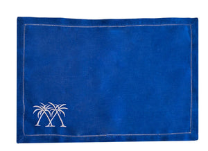 The Coastal Linen Placemat Set by Pink House Mustique features rectangular blue placemats with stitched edges and two white embroidered palm trees—ideal for bringing a beach-inspired touch to your dining space.