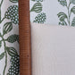 Close-up of the Rita Cane Wrap Four Poster Bed by Julian Chichester, featuring a cane-wrapped post next to a light upholstered headboard, set against green leaf-patterned wallpaper.