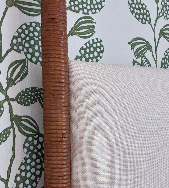 Close-up of the Rita Cane Wrap Four Poster Bed by Julian Chichester, featuring a cane-wrapped post next to a light upholstered headboard, set against green leaf-patterned wallpaper.