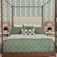 A neatly made Julian Chichester Rita Cane Wrap Four Poster Bed with green patterned bedding and pillows, flanked by two lamps on white nightstands against a leafy wallpaper background.