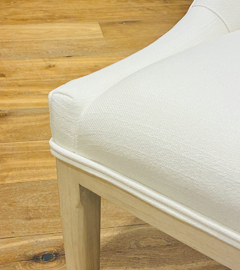 Close-up of the Maurice Dining Chair by Sherrill/Mr & Mrs Howard, showcasing elegant white upholstery and wooden legs on a light brown floor—ideal for stylish, comfortable seating.