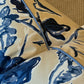 The Roses Blue and Cream Pillow by Hive Custom Pillows features a blue and white floral design with blue piping, crafted from premium materials, displayed on a textured beige surface.