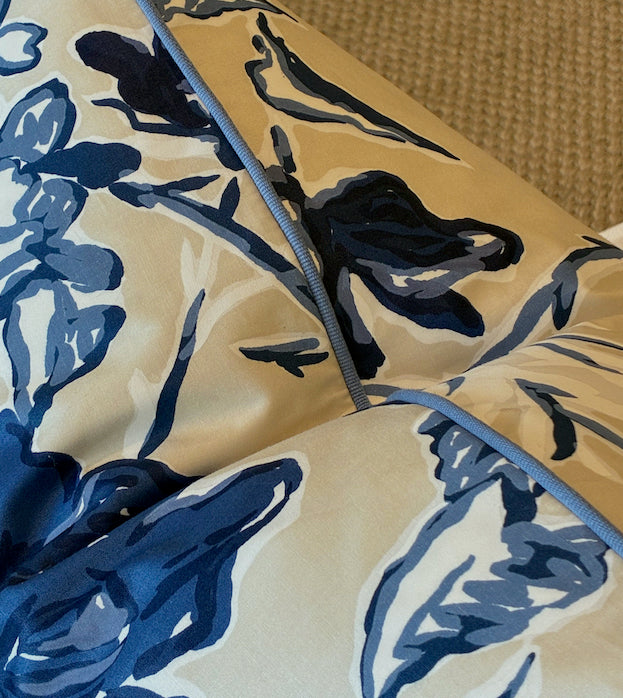 The Roses Blue and Cream Pillow by Hive Custom Pillows features a blue and white floral design with blue piping, crafted from premium materials, displayed on a textured beige surface.