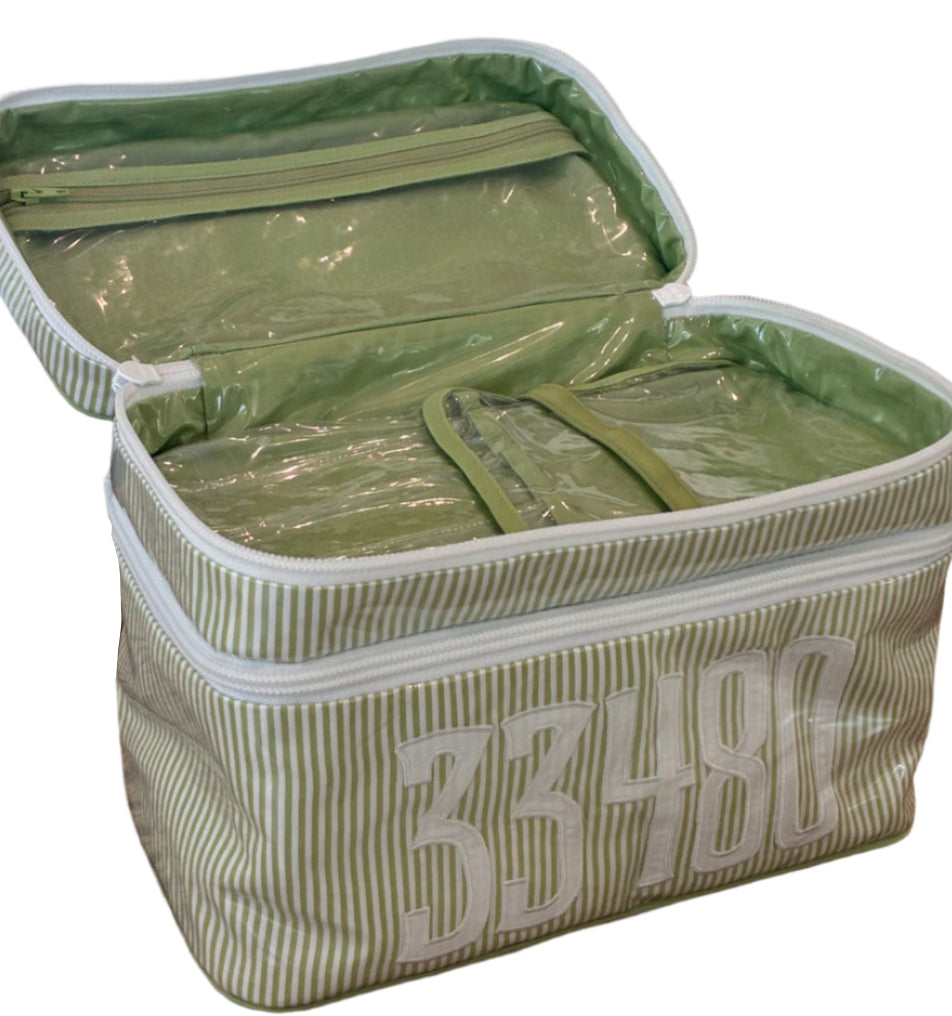 A green and white striped Walton Travel Case by Walker Valentine, featuring the number 33480 on the front and a secure double zipper, sits open on a wicker surface.